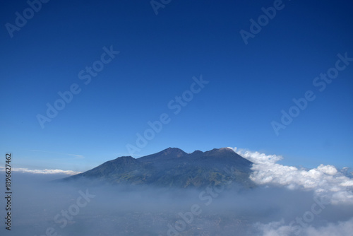 A mountaintop scene with white clouds enveloping it against a backdrop of a clear blue sky