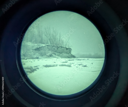 Winter maritime sea cliff and frozen shore viewed through authentic white phosphor night vision device for tactical coastal surveillance observation.