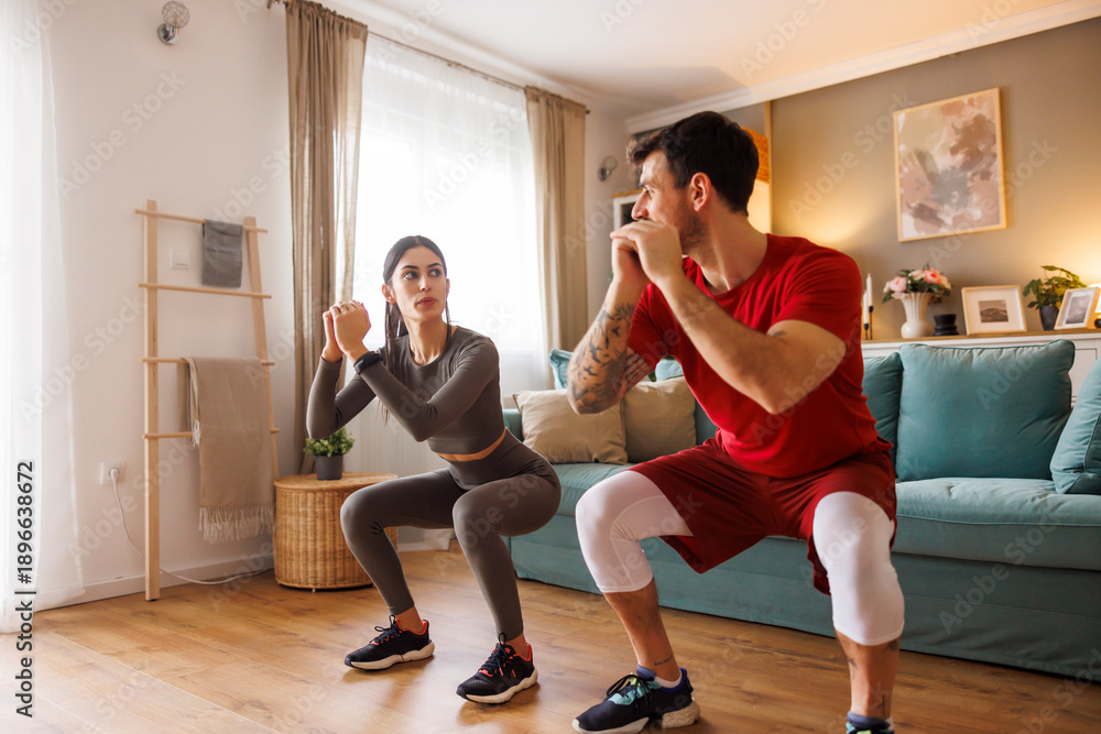 Obraz premium Active couple doing squats exercise while working out at home
