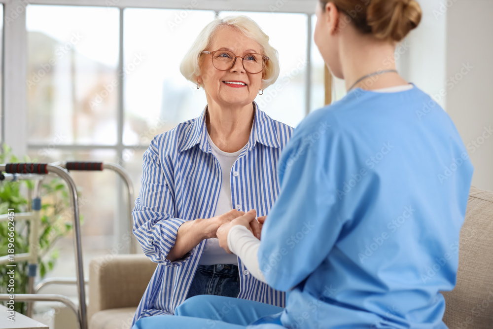 Fototapeta premium Caregiver and senior woman sitting on sofa in nursing home