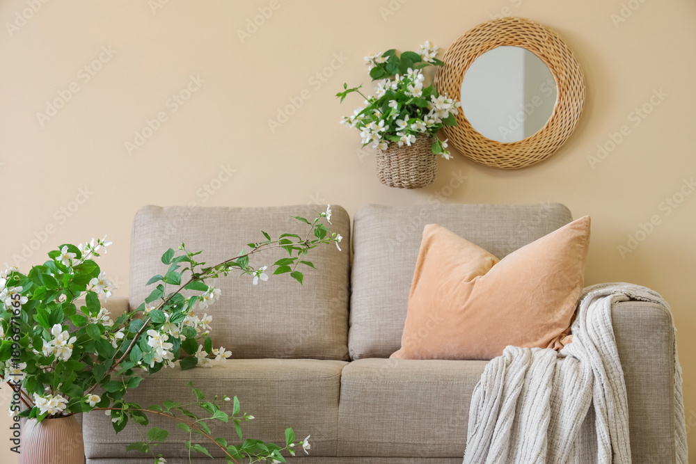 Naklejka premium Interior of living room with sofa and blooming jasmine flowers near beige wall, closeup