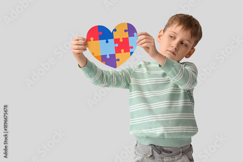 Little boy with autistic disorder and paper puzzle heart on white background