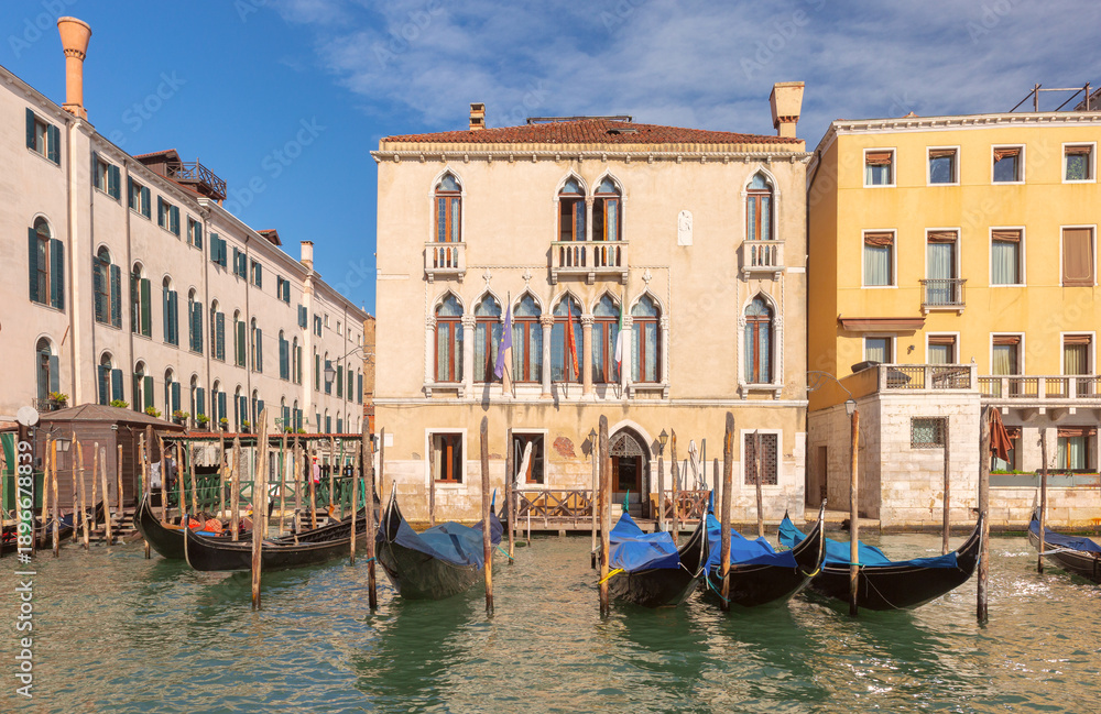 Fototapeta premium Colorful historic buildings line the edge of a canal in Venice, Italy, with arched windows, balconies, and mooring poles.