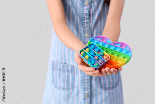 Foto Cute girl with autistic disorder and pop it fidget toys on light background, clo