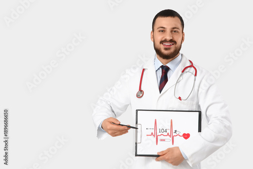 Young happy male doctor pointing at clipboard with cardiogram on white backgr...