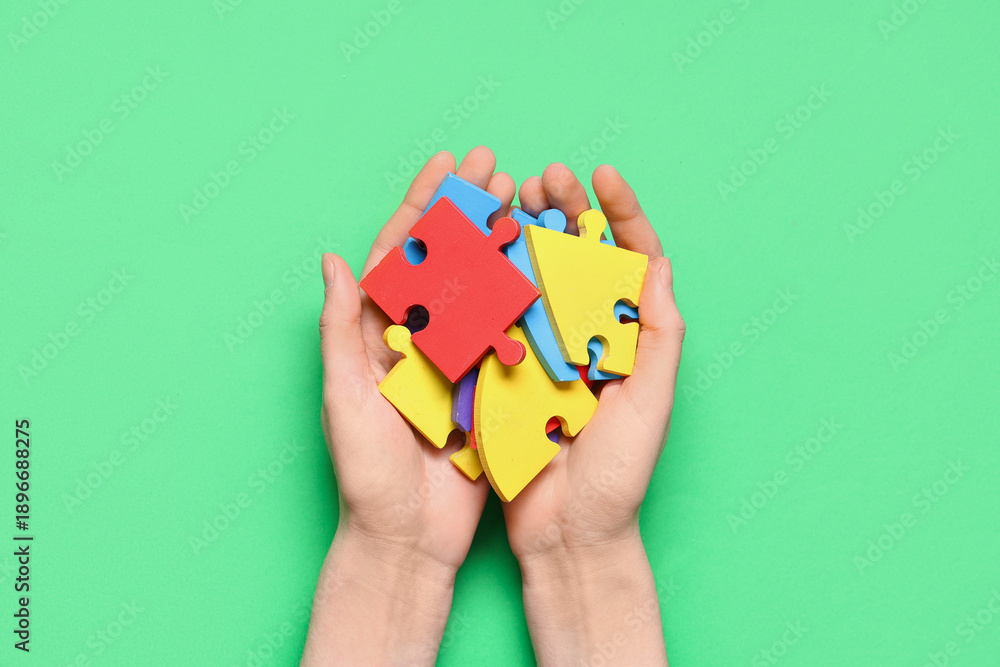 Fototapeta premium Female hands with colorful puzzle pieces on green background. Autistic disorder concept