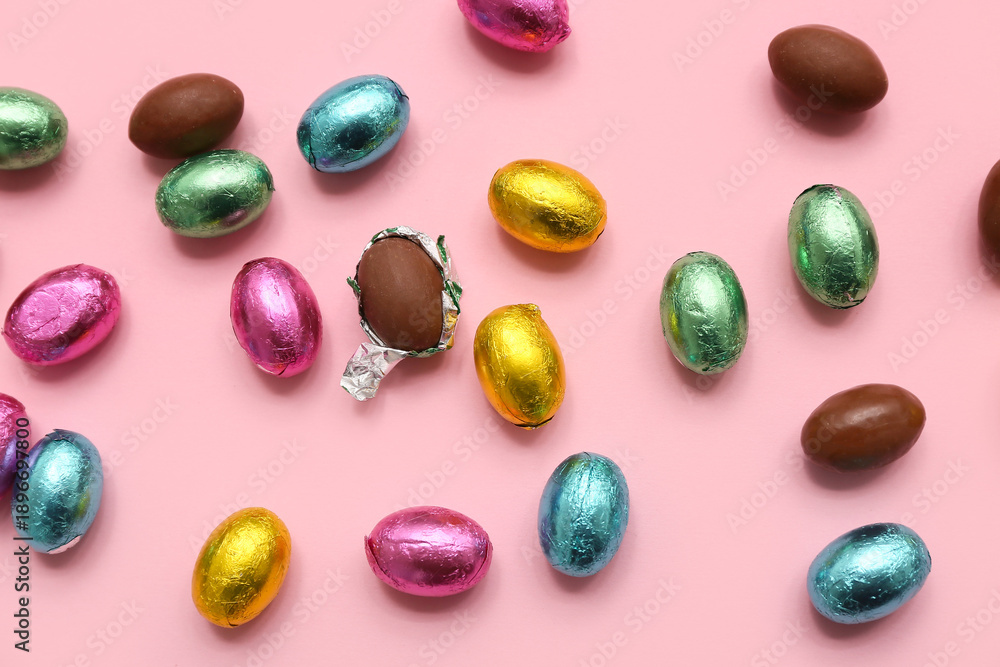 Fototapeta premium Unpacked and wrapped chocolate Easter eggs in foil on pink background