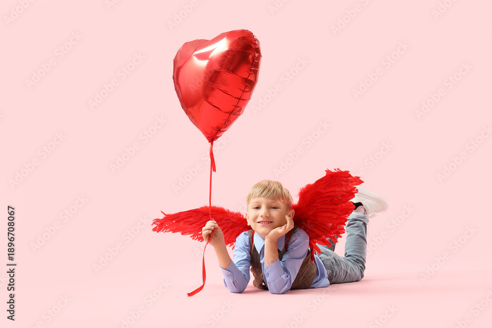 Obraz premium Cute little happy boy in cupid wings with heart-shaped balloon lying on pink background. Valentine's Day celebration
