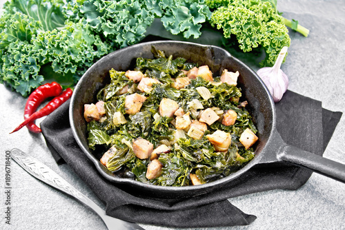 Kale cabbage with bacon in pan on gray stone