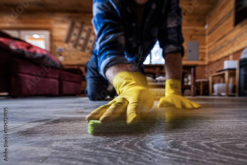 A low-angle, detailed shot of a person wearing bright yellow protective rubber gloves while cleaning a modern wood-laminate floor.