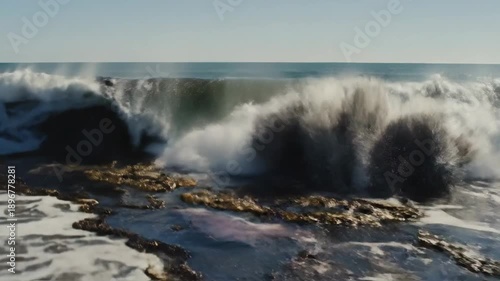 Wallpaper Mural A powerful ocean wave breaks with shimmering crest against rugged rocks on a sunny day Torontodigital.ca