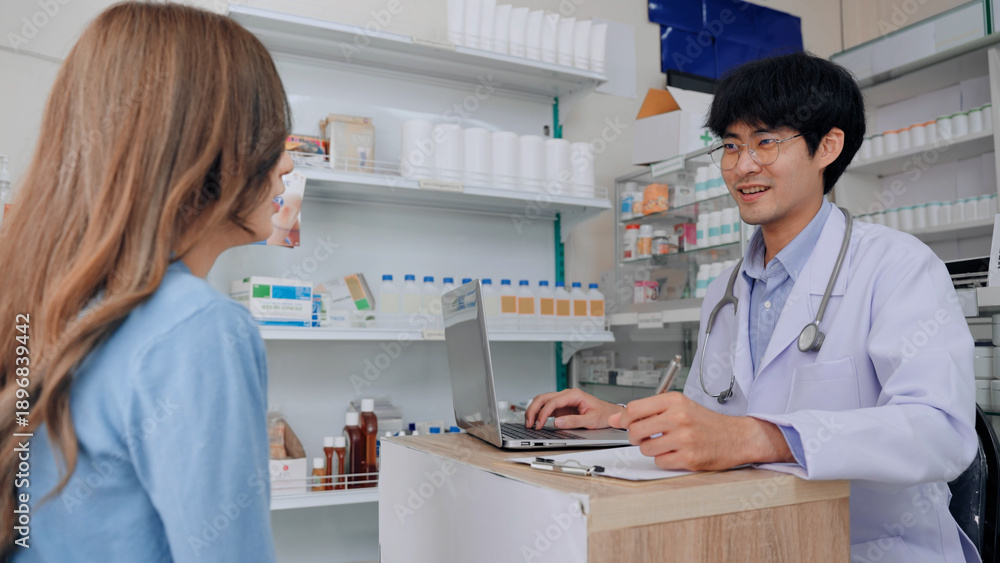 Fototapeta premium A professional Asian male pharmacist in a white lab coat consults a female patient in a modern drugstore. This medical depicts expert healthcare service and patient care
