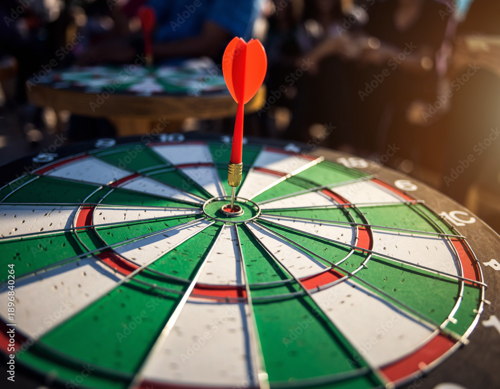 Fototapeta premium A red dart hits the bullseye of a green and white target, showcasing the instant of concentration and proficiency in a sociable contest. The atmosphere buzzes with exhilaration and expectation.