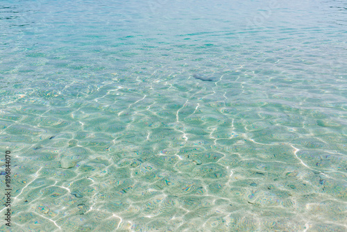 The surface of clear turquoise water with sun glare. Relaxation and tranquility on vacation. Space for text. Background.