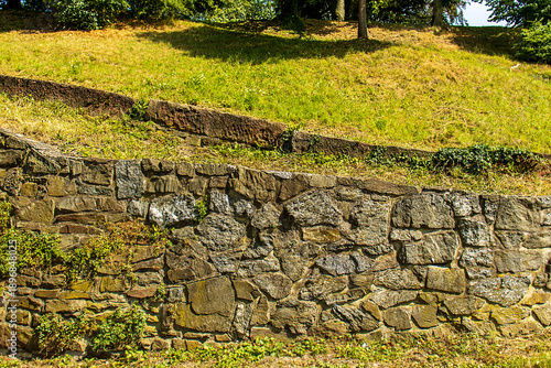 Canvastavla Old stone retaining wall in a public park with green grass and trees on a sunny