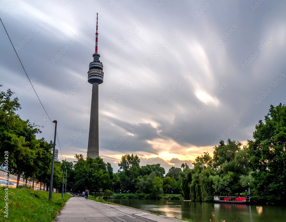 Naklejka premium A tall tower stands beside a serene river and walkway