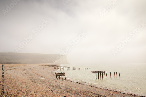 Mist Over a Quiet Seaside With Ruined Docks and Cliffs Along a Pebble Beach