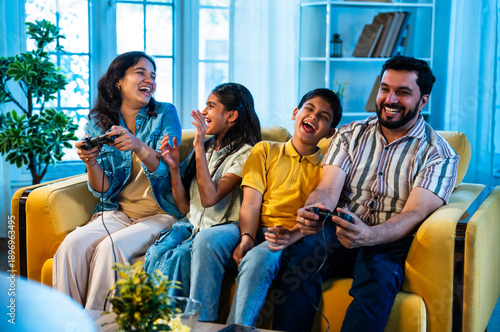 Indian parents and kids enjoying competitive video gaming together on sofa at home