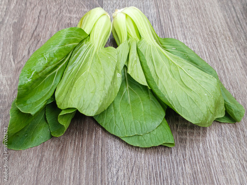 Fresh bok choy vegetables on wooden background, top view composition with water drops, showing organic leafy greens, healthy food ingredients, and natural texture with copy space.