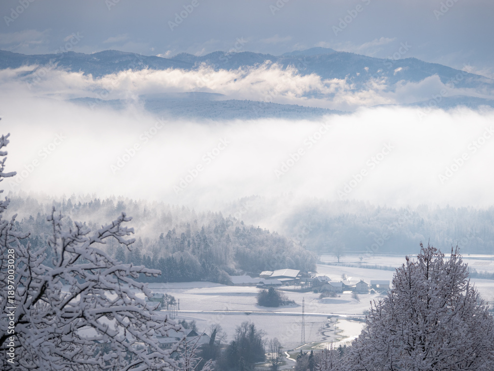 Fototapeta premium Misty clouds rolling over forest and hilly countryside after freshly fallen snow