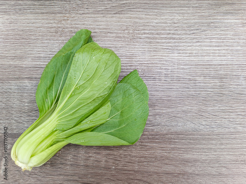 Fresh bok choy vegetables on wooden background, top view composition with water drops, showing organic leafy greens, healthy food ingredients, and natural texture with copy space.