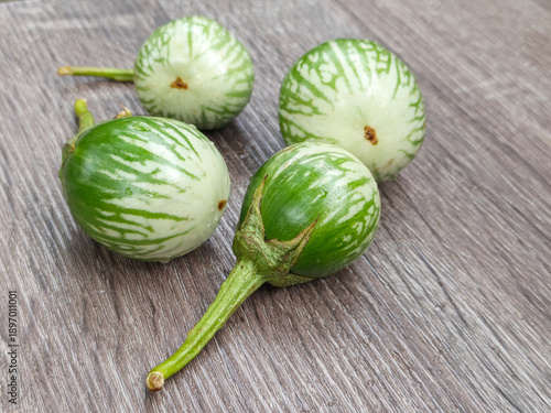 Fresh green striped eggplants on wooden surface, close-up view showing natural texture and pattern, raw organic vegetables used in Asian cuisine with rustic background