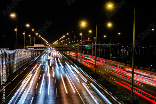 Night traffic on highway with dynamic car light trails and street lamps in the city.
