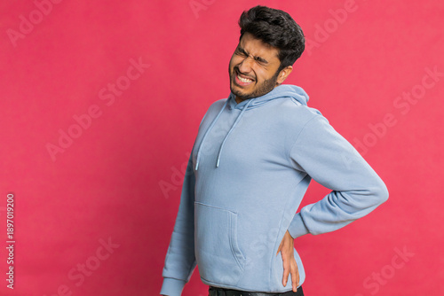 Fotografija Indian man suffering backache, massaging sore place lower spine, frowning from unbearable spasm torn muscles and tendons, kidney stones pinched nerve