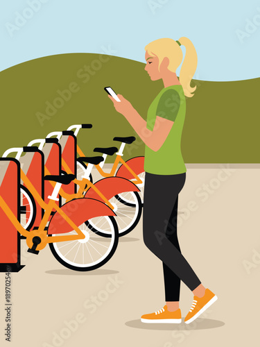 Young woman using smartphone to rent orange bicycle at bike share station for eco friendly urban transportation and recreation healthy lifestyle concept in city park environment for sustainable travel