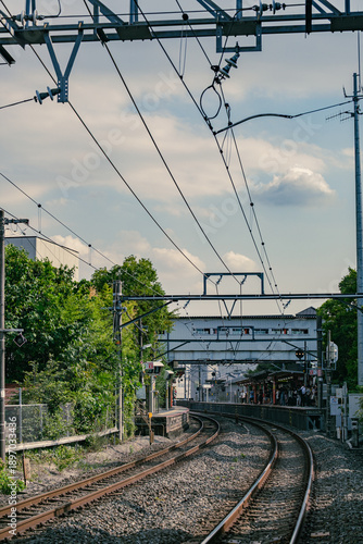 Japanese railway station platform and tracks with overhead wires in residential area.