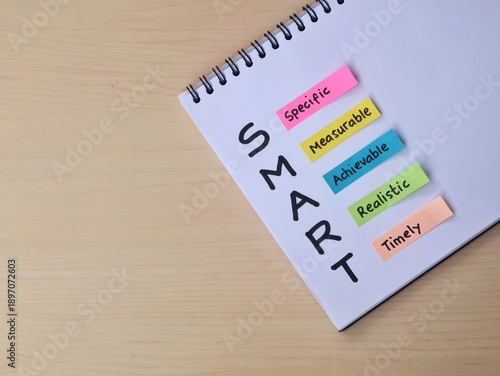 SMART Goals framework concept on book with colorful adhesive notes on wooden desk. Ideal for business planning and personal development