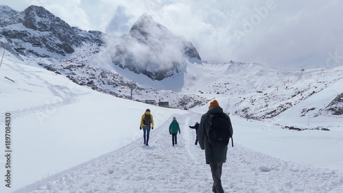 Fotografie Hikers trek uphill on a groomed snowy trail toward a cloud-veiled mountain summi