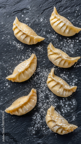 Raw handmade stuffed dumplings sprinkled with flour on black slate background