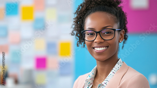 Close-up of a nonprofit office assistant smiling at camera, colorful mission statement wall softly blurred, desk with clipboard and ID badges in focus