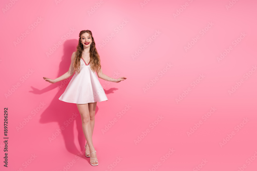 Obraz premium Young woman in a white dress posing playfully, showcasing elegance and style against a vibrant pink background