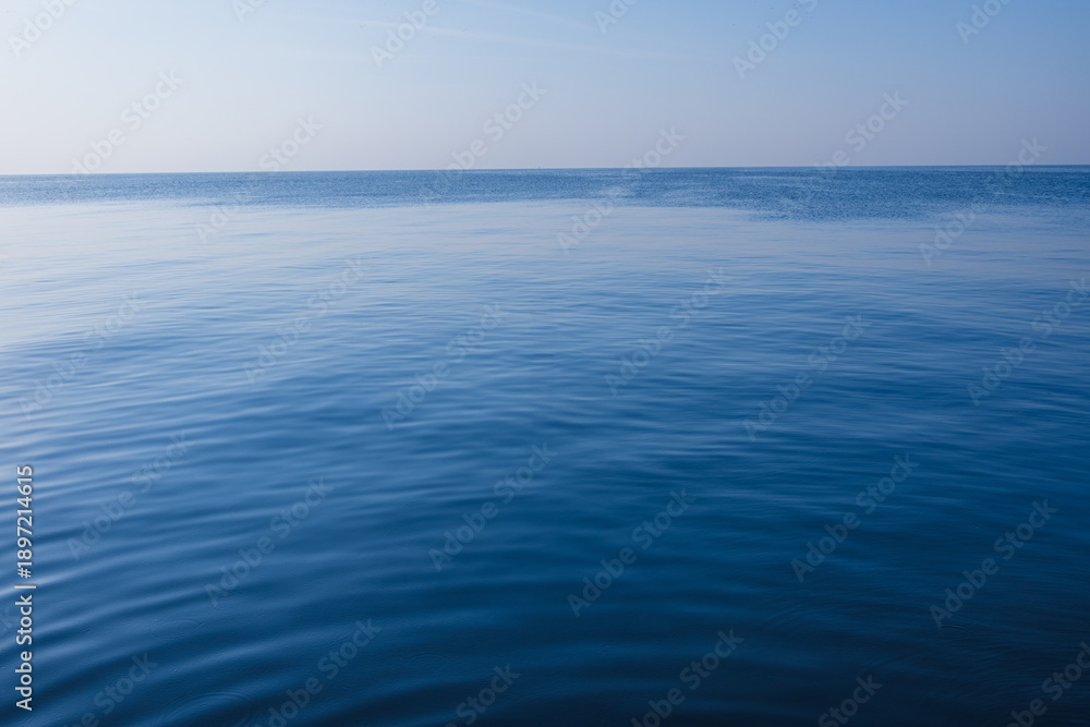Fototapeta premium Calm Deep Blue Ocean Surface with Soft Ripples under Clear Sky,A serene and minimalist view of a vast, calm blue sea with gentle ripples on the water surface stretching to the horizon under a clear,