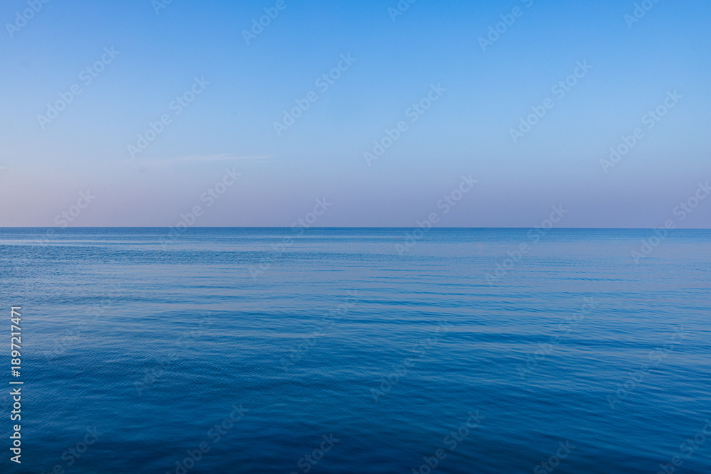 Obraz premium Calm Deep Blue Ocean Surface with Soft Ripples under Clear Sky,A serene and minimalist view of a vast, calm blue sea with gentle ripples on the water surface stretching to the horizon under a clear,