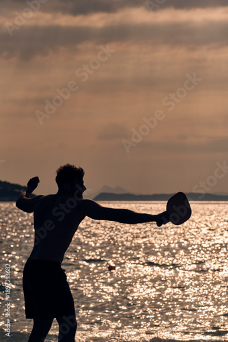 Uomo che gioca a racchettoni in controluce al tramonto sul mare