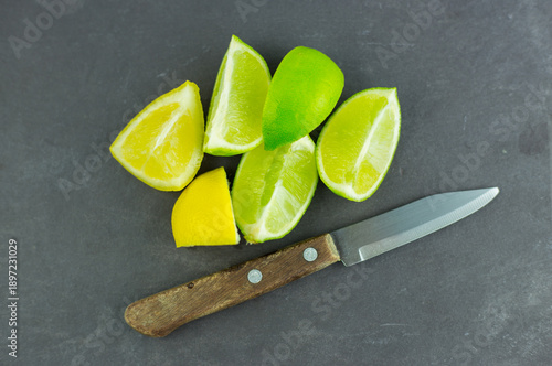 Wedges of lemon and lime with a small knife set on a grey slate cutting board. Concept: for use in the preparation of drinks and cocktails.