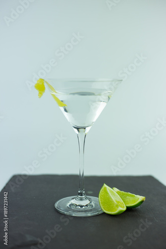 A vesper martini in a traditional martini glass set on a grey slate chopping board with wedges of lime against a white background