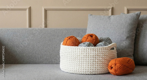 Close-up of a white woven basket filled with orange and gray balls on a gray couch with a beige wall in the background.