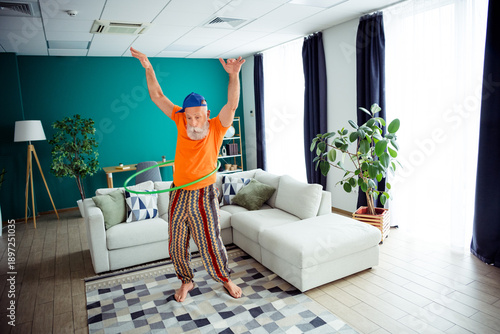 Photos Playful grandpa hula hoops indoors in a cozy living room wearing bright orange s