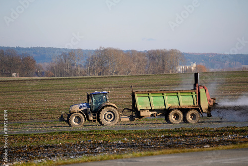 Tableau sur toile Modern blue tractor pulling a manure spreader trailer, fertilizing a farm field under a clear blue sky