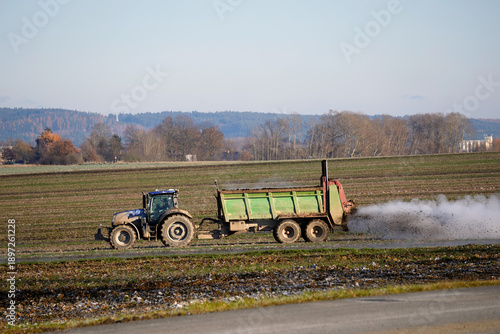 Photos Modern blue tractor pulling a manure spreader trailer, fertilizing a farm field under a clear blue sky