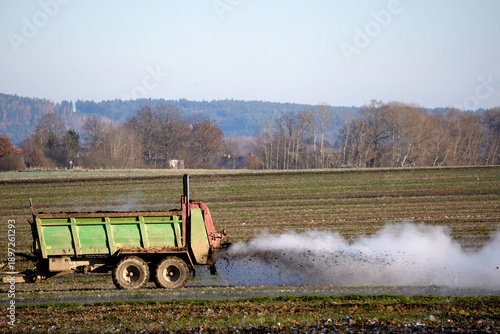 Tableau sur toile Modern blue tractor pulling a manure spreader trailer, fertilizing a farm field under a clear blue sky