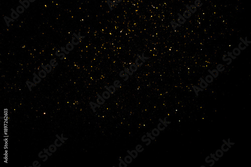 Shimmering gold flakes, sparkling gold particles on a black background. Tiny material for backgrounds or textures in art designs.
