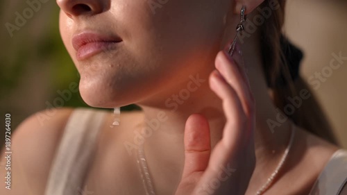 Close-up video of an attractive young woman's neck and jawline. She is gently touching her earring and skin, enjoying the warm sunlight