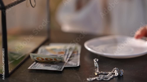 Unrecognizable person accepts a cash payment, possibly a bribe, over coffee. Focus is on the stack of hundred-dollar bills and jewelry