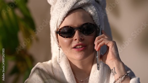 Beautiful young woman wearing a bathrobe, towel on her head, and sunglasses happily talking on her cell phone on a sunny day