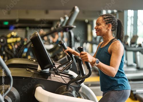 Portrait of a young black woman exercising on an elliptical trainer in a gym, running using  thereadmill machine equipment, healthy lifestyle and cardio exercise at fitness club concepts